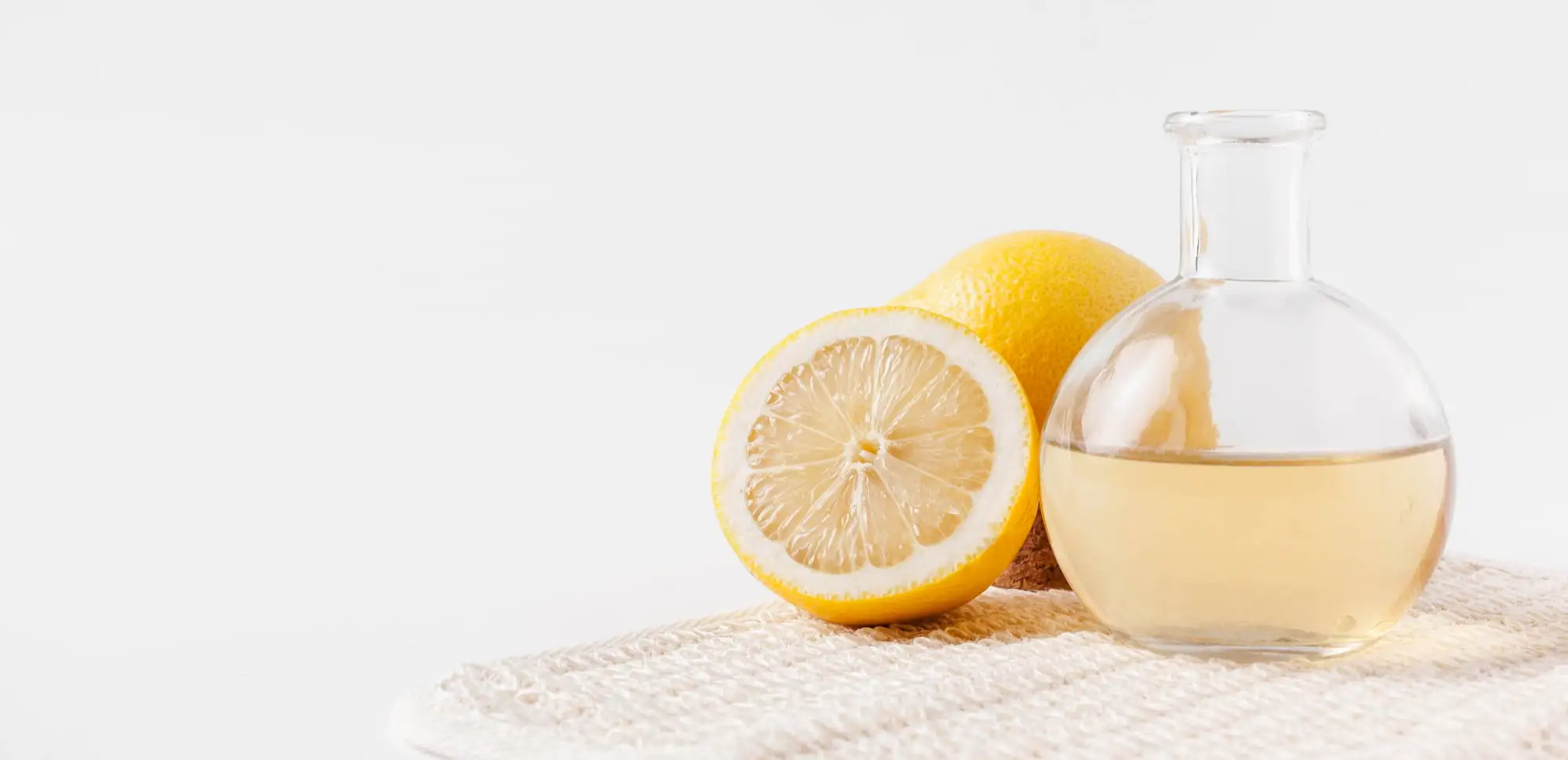 Bottiglia di aceto in vetro e limone tagliato a metà su una superficie bianca utilizzata per soluzioni detergenti naturali