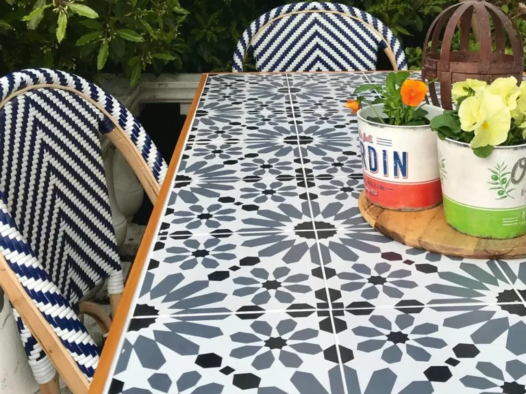 Outdoor ceramic tile table with a blue and white geometric design flanked by striped chairs and potted plants