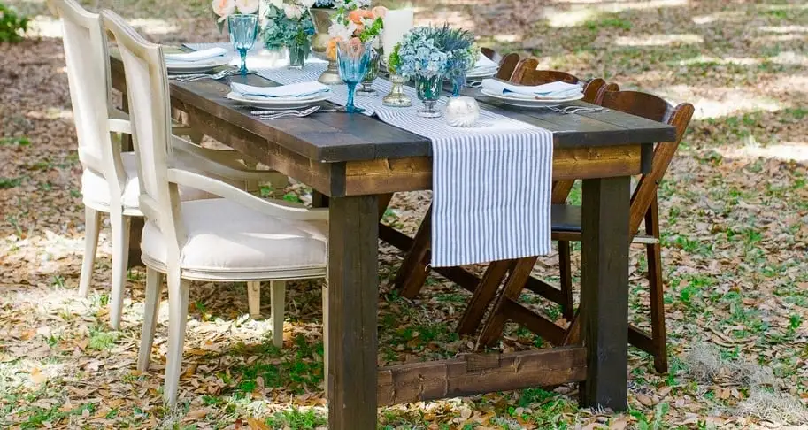 Outdoor setup with a rustic farmhouse dining table elegantly set for a meal under the trees