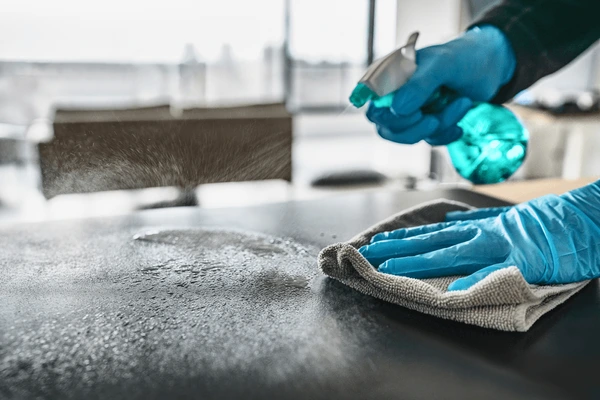 Person wearing blue gloves cleaning a surface with a spray bottle and cloth