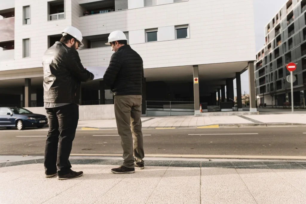 Two contractors in hard hats discussing plans outside an apartment building