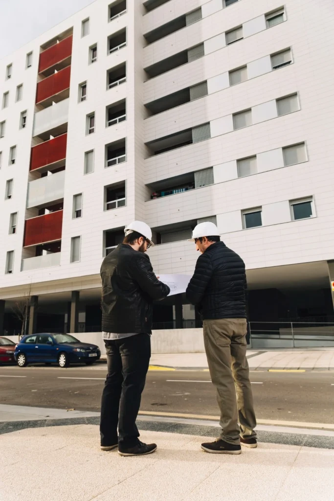 Two contractors reviewing blueprints outside a high rise apartment building