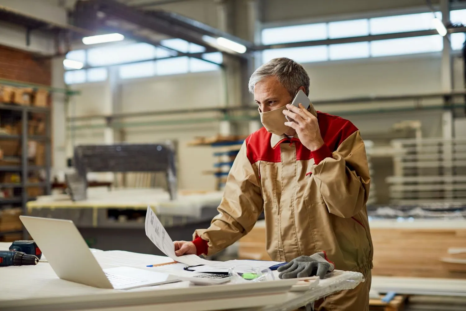 Worker in a factory planning production schedule while talking on the phone and reviewing documents