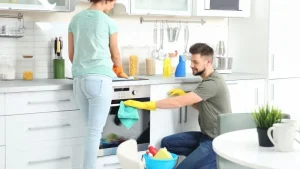 Couple cleaning the kitchen together with one wiping the oven and the other cleaning the countertop