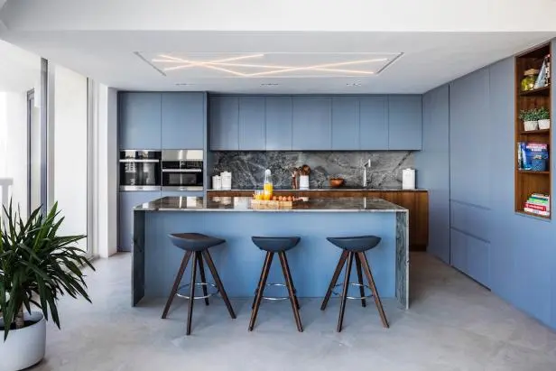 Hidden appliances in modern kitchen cabinets with blue finishes and sleek island design Hidden appliances in modern kitchen cabinets with blue finishes and sleek island design