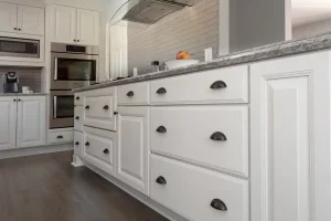 Mobili da cucina bianchi con maniglie a tazza scure e piano di lavoro grigio