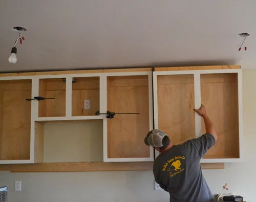 Worker installing wooden kitchen cabinets on the wall Worker installing wooden kitchen cabinets on the wall