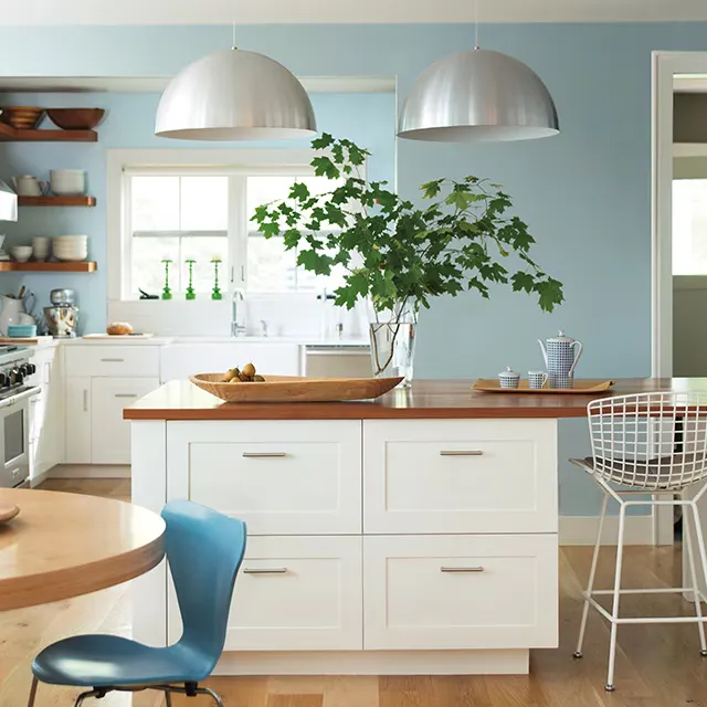Bright kitchen with white cabinets light blue walls and large pendant lights