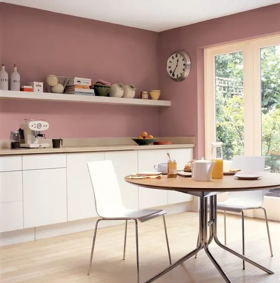 Minimalist kitchen with white cabinets and a soft pink wall in the dining area