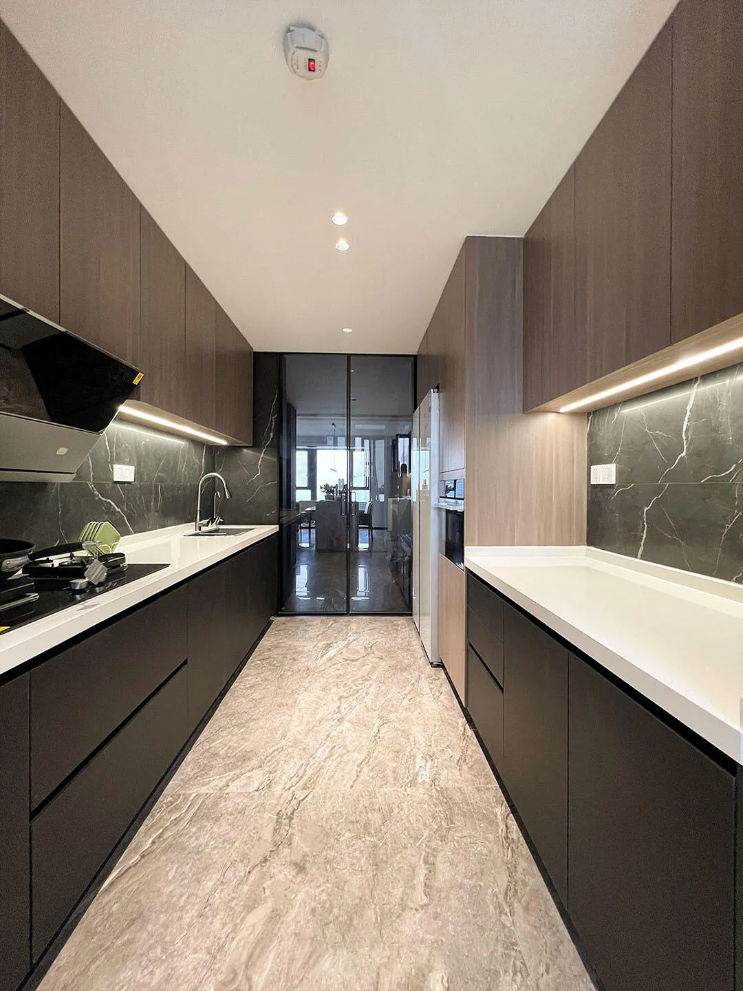 Narrow galley kitchen with dark wood cabinets and marble flooring