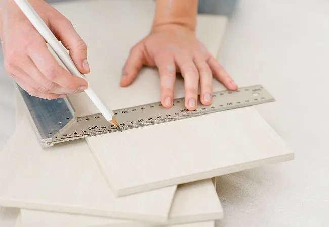 Person marking plywood board with ruler and pencil Person marking plywood board with ruler and pencil