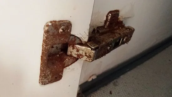 Severely rusted cabinet hinge on white door interior Severely rusted cabinet hinge on white door interior