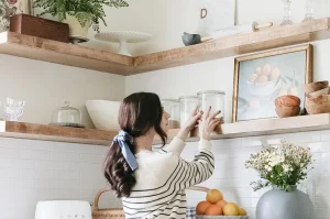 Woman organizing kitchen items on open shelve